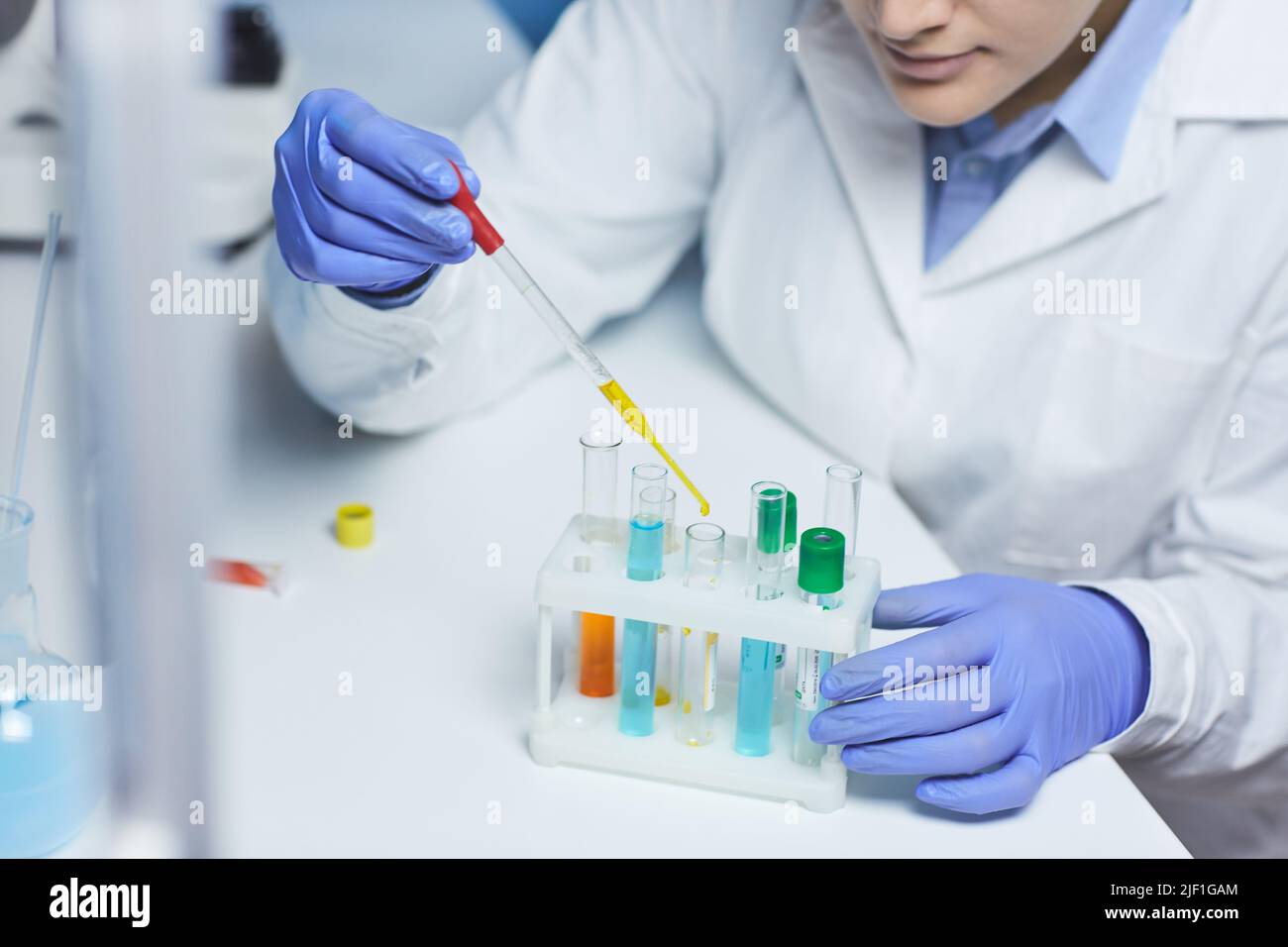 Primo piano di un'intensa farmacia femminile in guanti di gomma blu seduti alla scrivania in laboratorio Foto Stock