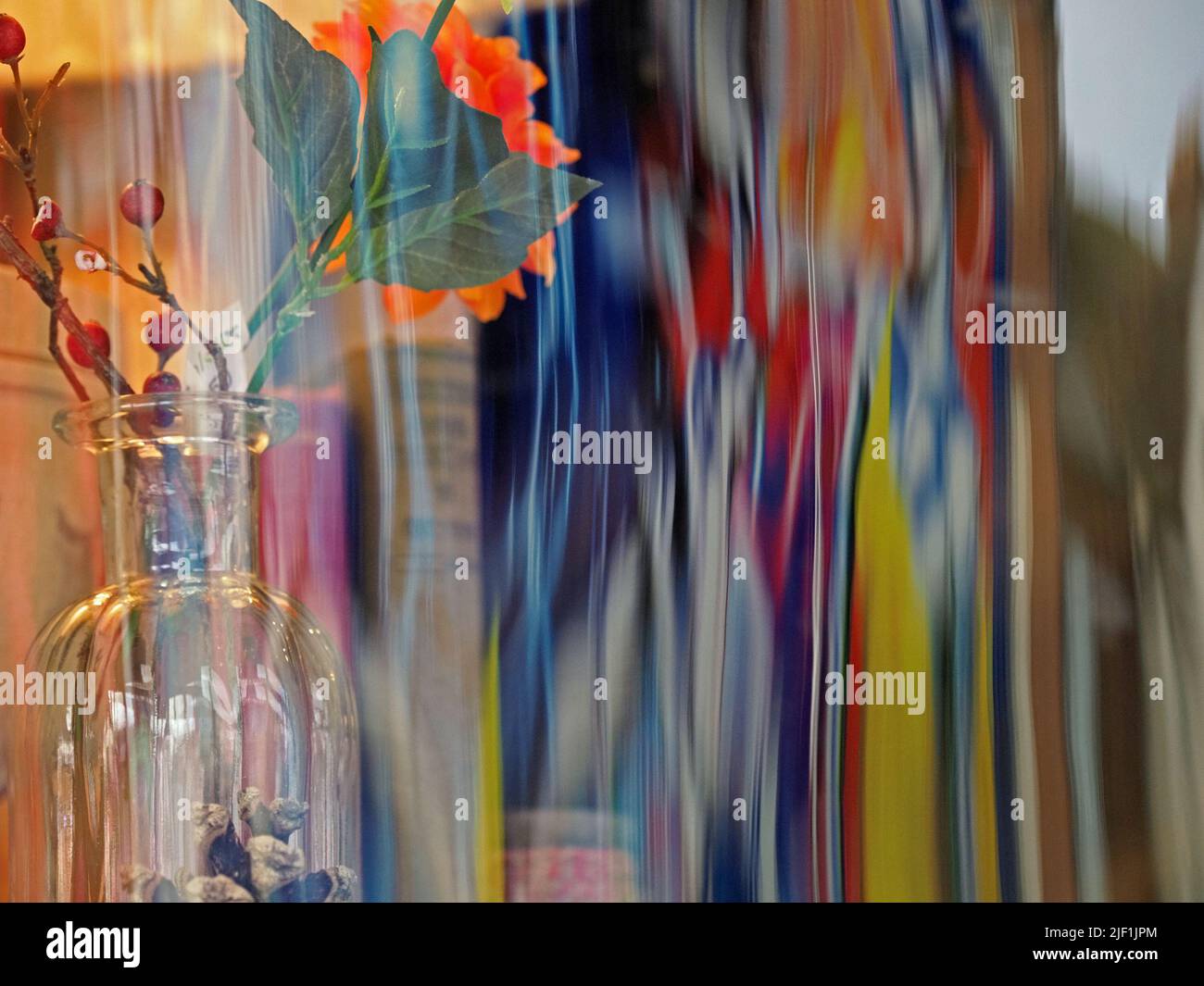 Bottiglia di vetro con display floreale dietro colorati riflessi distorti in vetro curvo finestra in Wiltshire, Inghilterra, Regno Unito Foto Stock