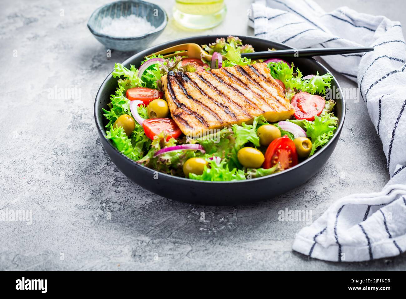 Insalata fresca con formaggio alla griglia, pomodori e olive sul grigio Foto Stock