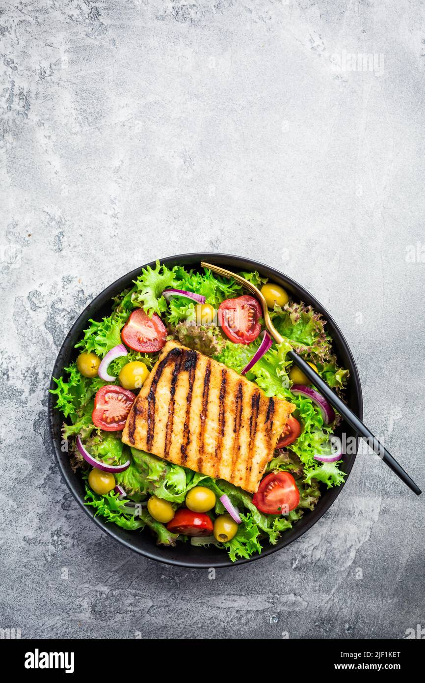 Insalata fresca con formaggio alla griglia, pomodori e olive sul grigio Foto Stock