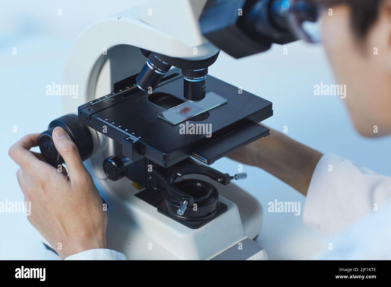 Scienziato in occhiali seduti alla scrivania in laboratorio e utilizzando il microscopio durante lo studio delle molecole Foto Stock