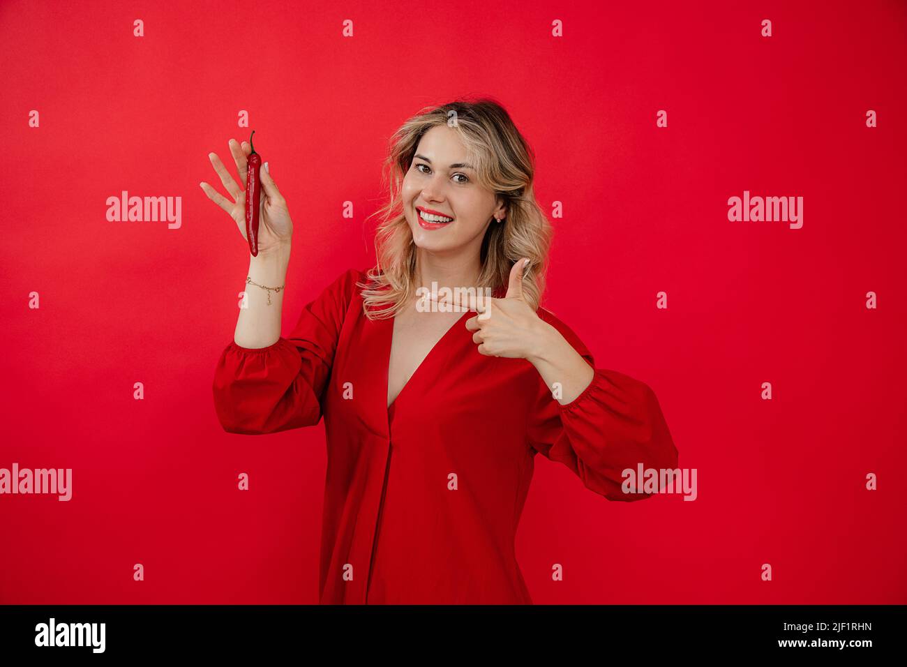 Giovane donna cliente promotore femminile, abito rosso, peperoncino caldo in mano sorriso, puntando dito copia spazio per le notizie Foto Stock
