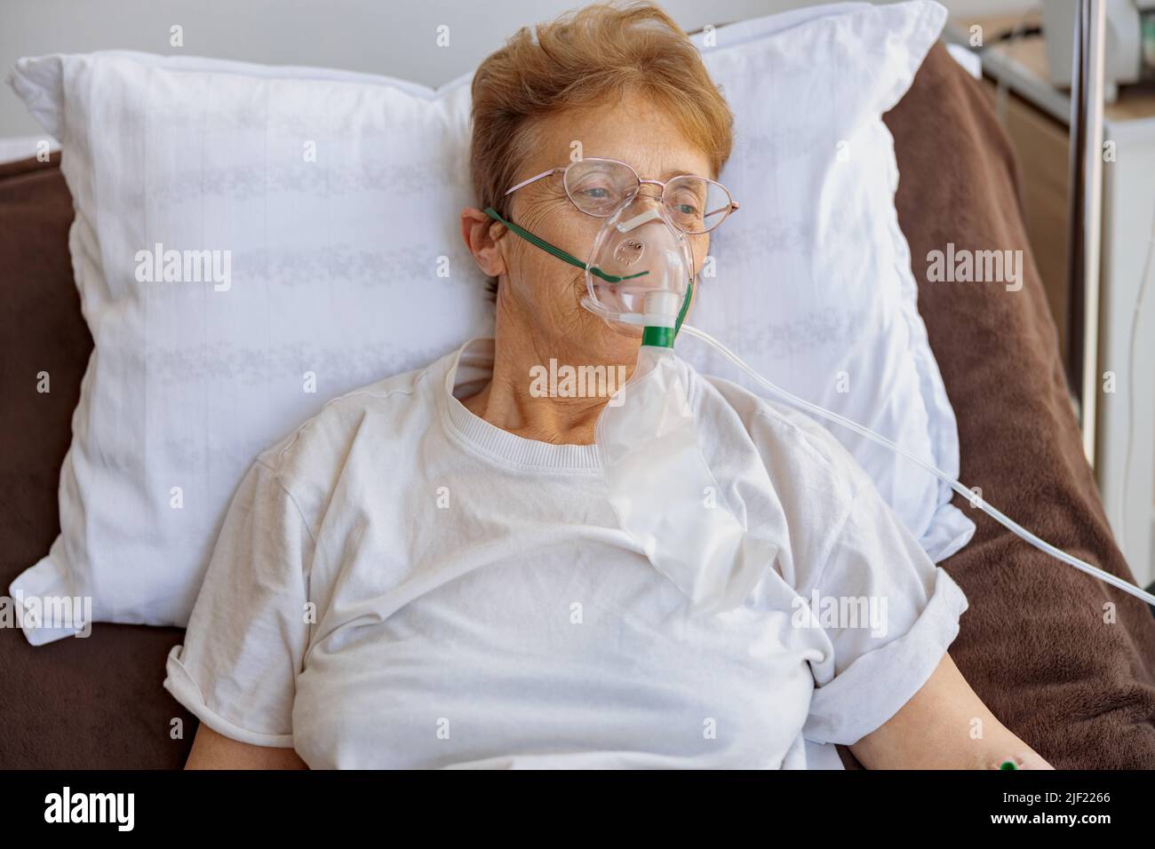 La paziente anziana in una maschera respiratoria si trova nel reparto durante il trattamento per Covid-19 Foto Stock