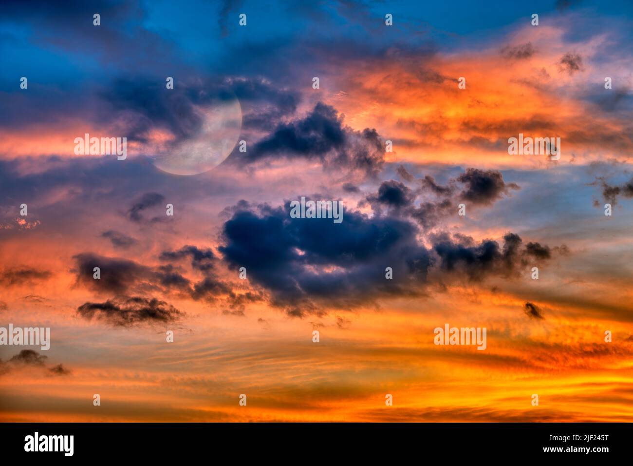 La Luna sta risplendente tra Un colorato cielo di Tramonto riempito di nube Foto Stock