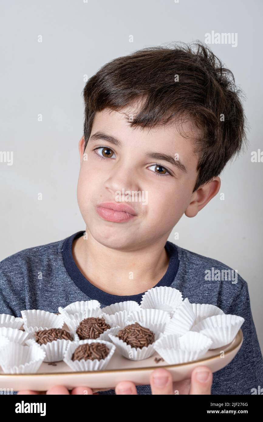 Bambino di 9 anni che tiene un vassoio con palle di fudge brasiliane e facendo un viso dubbioso. Foto Stock