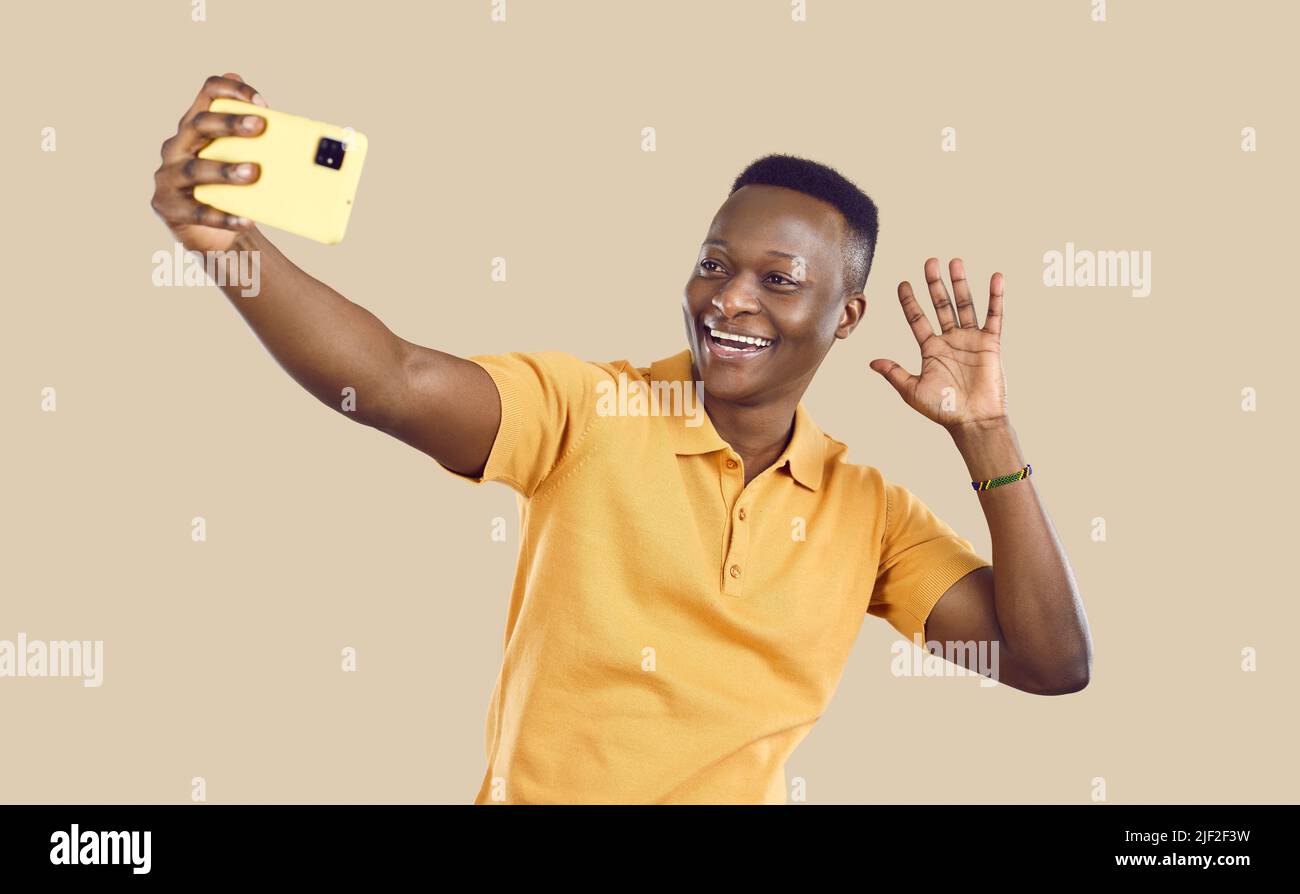 Felice uomo africano che sventola ciao come prende selfie o fa videochiamata sul telefono cellulare Foto Stock