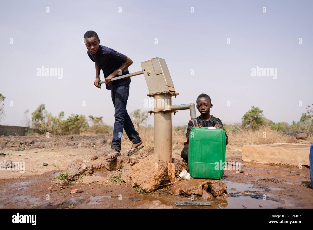 Due ragazzi africani si occupavano di riempire contenitori d'acqua ad una pompa remota del villaggio; scarsità d'acqua nel concetto dei paesi in via di sviluppo Foto Stock