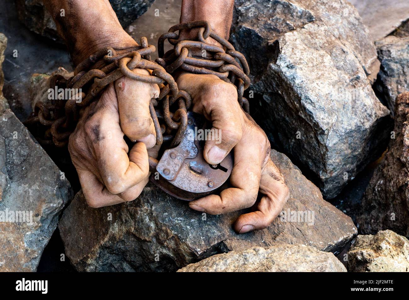 Uomo con le mani in mano sono concatenate. Grande vecchio castello di ferro. Grandi pietre grigie. I sottili e le mani sporche di un slave avvolto in una vecchia catena arrugginita Foto Stock