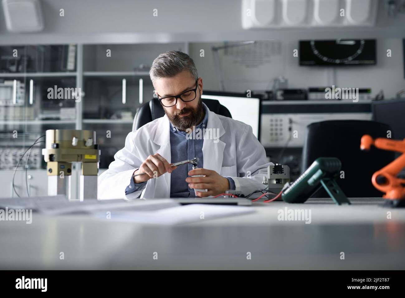 Ingegnere robotico che lavora alla progettazione di un moderno braccio robotico e seduto alla scrivania in laboratorio. Foto Stock