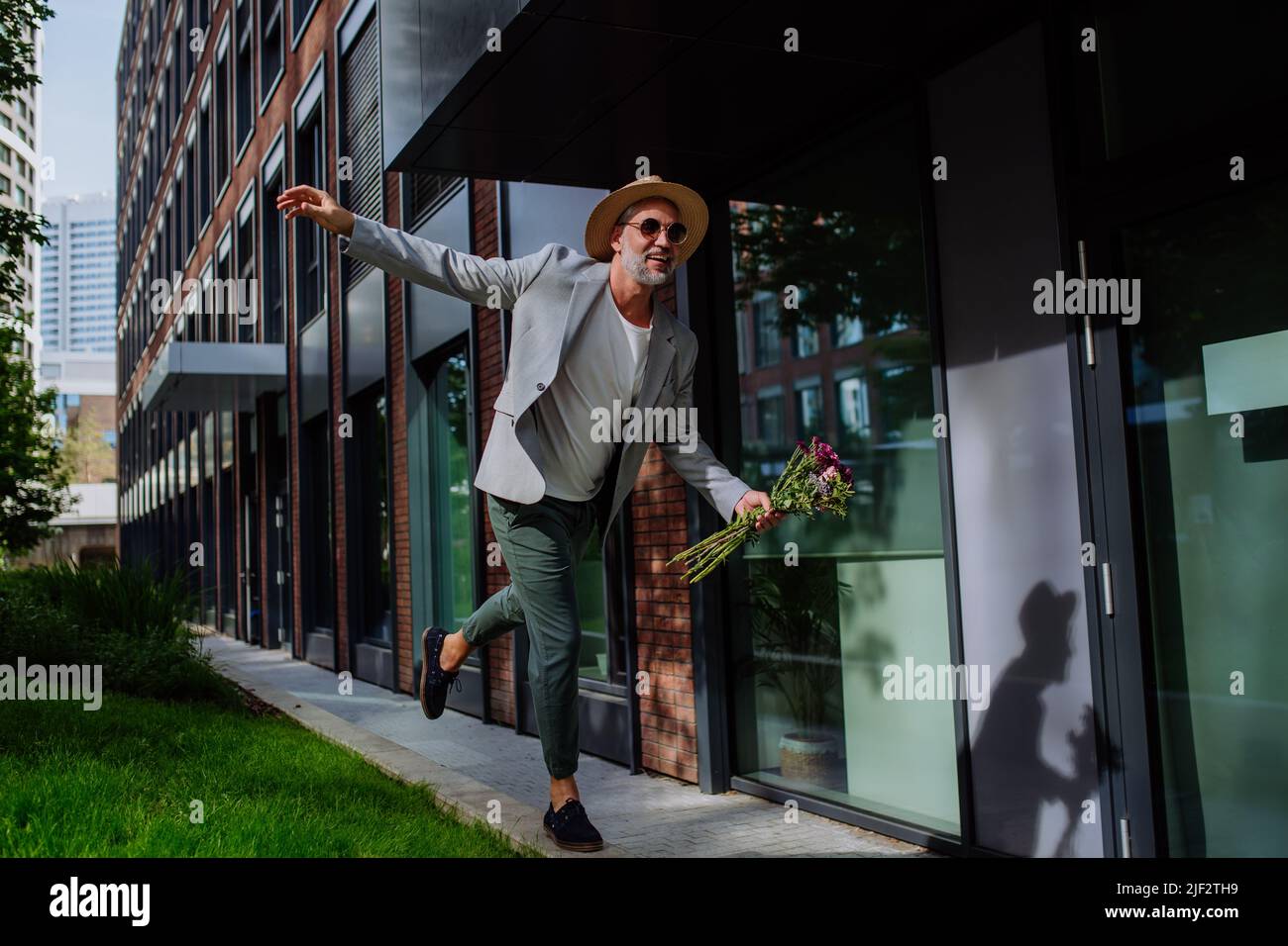 Ritratto di uomo maturo energico felice con bouquet di fiori in equilibrio sul muro , sensazione di libertà, concetto di equilibrio di vita. Foto Stock