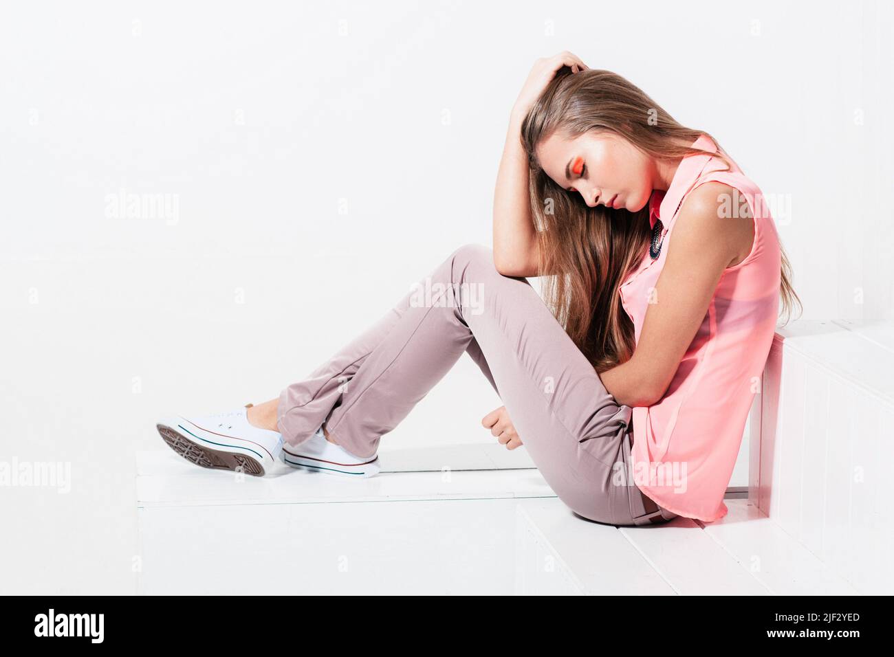 La ragazza pensiva è seduta su sfondo bianco Foto Stock