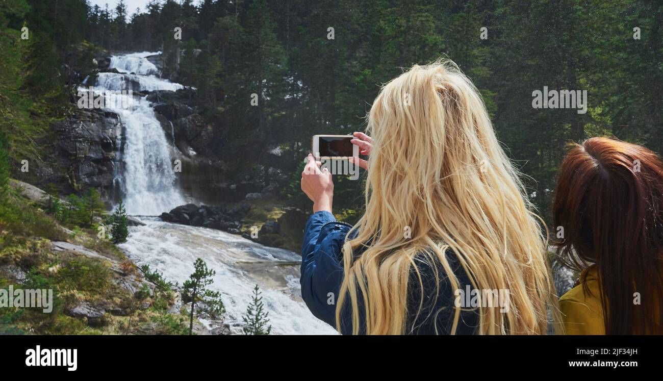 Donna fotografando una cascata sul suo cellulare durante un'escursione in natura con un amico.due donne su un'escursione in natura insieme prendendo una foto di un Foto Stock