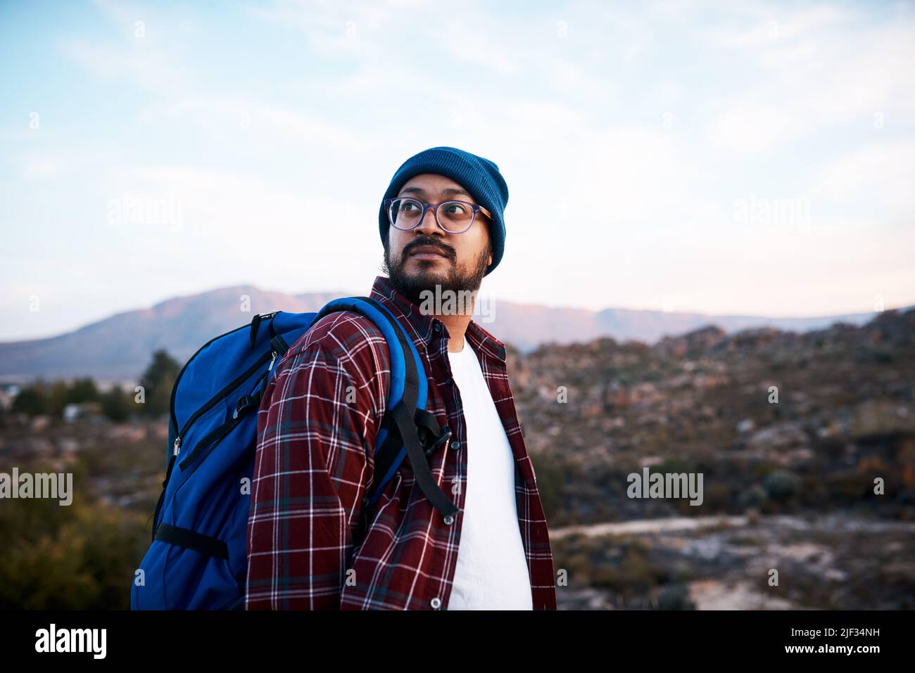 Un uomo escursionista guarda indietro al sentiero mentre zaino in spalla in montagna Foto Stock