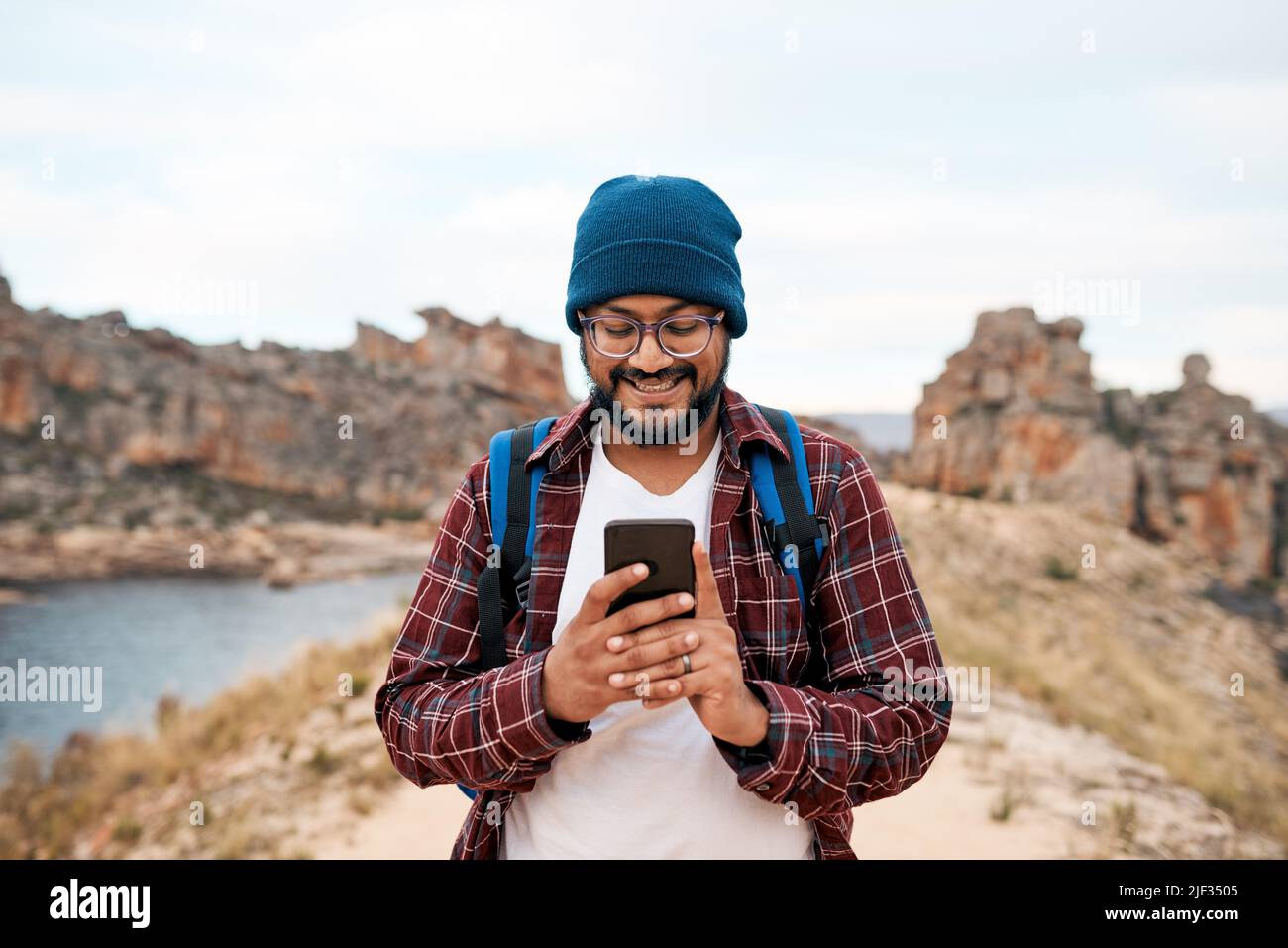 Un uomo attraente sorride al suo smartphone mentre si fa un'escursione nella natura selvaggia rocciosa Foto Stock