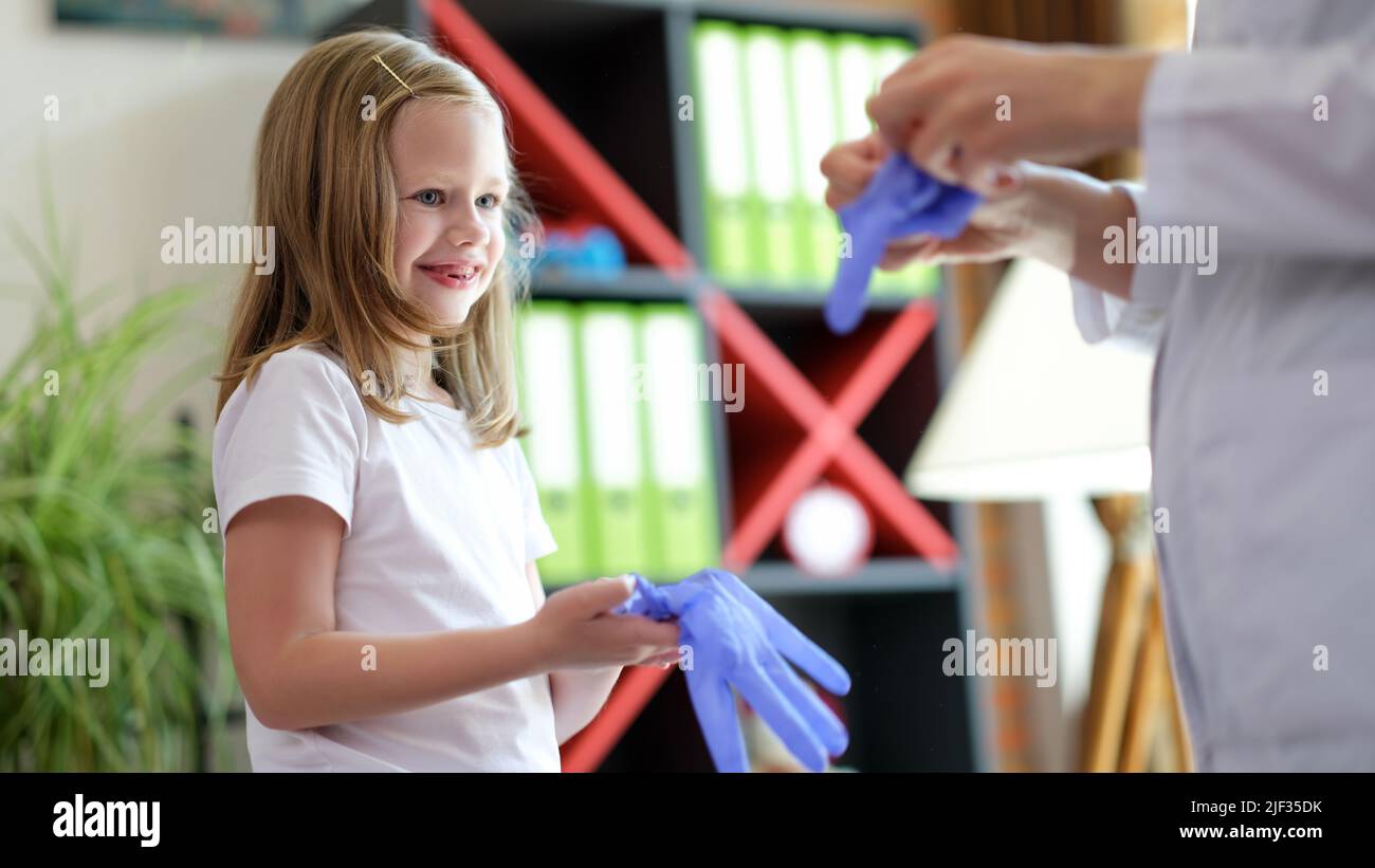 Medico e bambino di ragazza messo su guanti medici in clinica Foto Stock