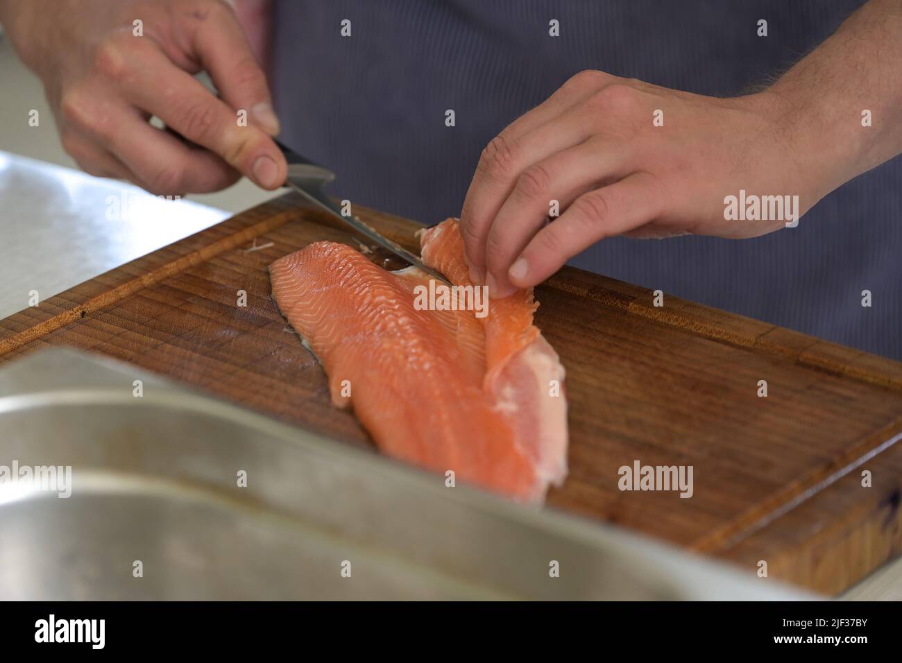 Preparazione del pesce char, le mani di un cuoco rimuovono il lembo della pancia con le ossa con un coltello di filettatura su un tagliere, fuoco selezionato, profondità stretta del fie Foto Stock