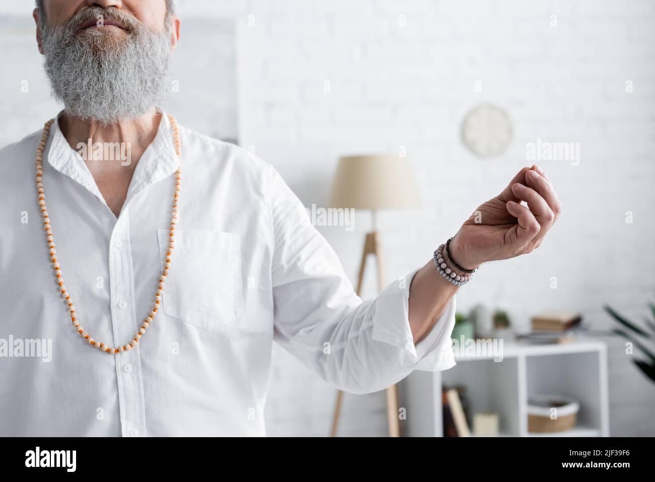 vista croppata dell'uomo del guru in perline che mostra mudra del mento mentre meditating a casa Foto Stock