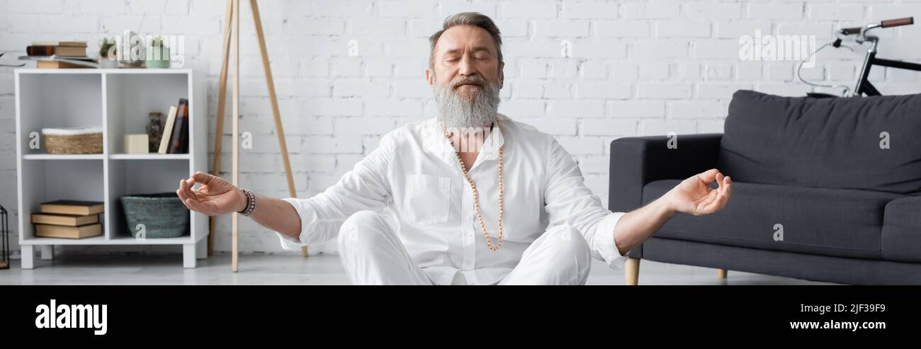 guru padrone bearded che mostra il mudra del mento mentre prega con gli occhi chiusi, bandiera Foto Stock