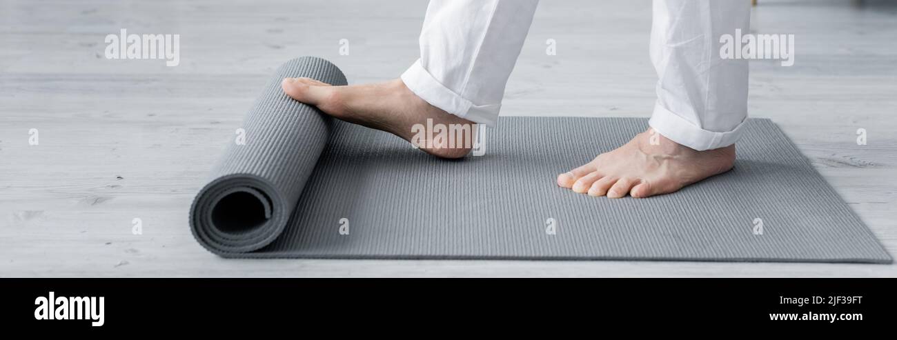vista ritagliata del maestro guru che srotola stuoia yoga, banner Foto Stock