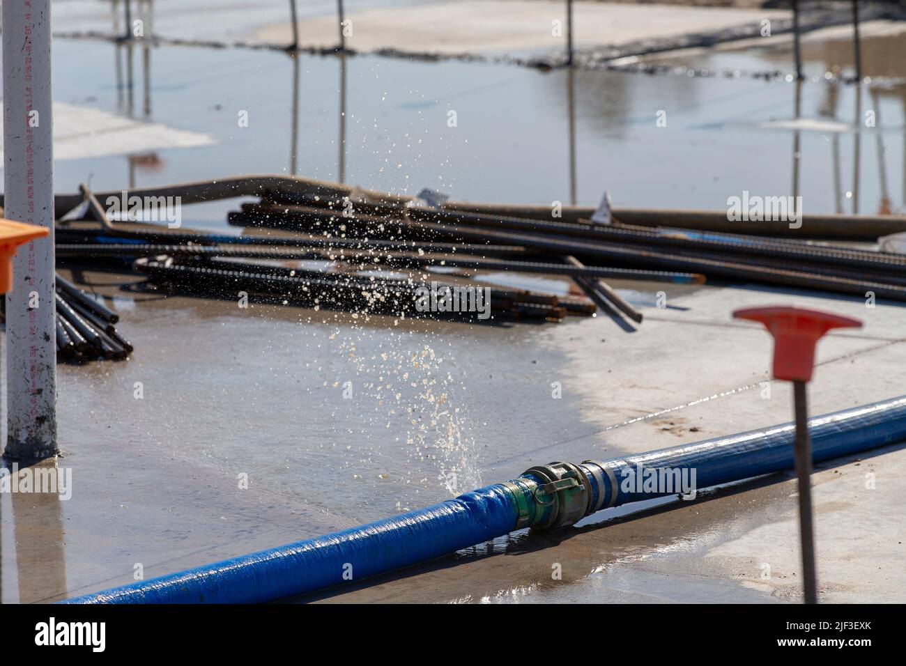 un tubo flessibile di acqua che perde su un cantiere da una pompa per svuotare una grande pozzanghera dopo un pesante rainstorm. waterpump firehose Foto Stock