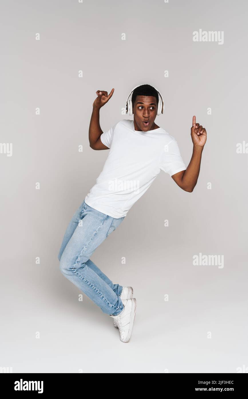 Giovane uomo nero che balla mentre ascolti la musica con cuffie isolate su una parete bianca Foto Stock