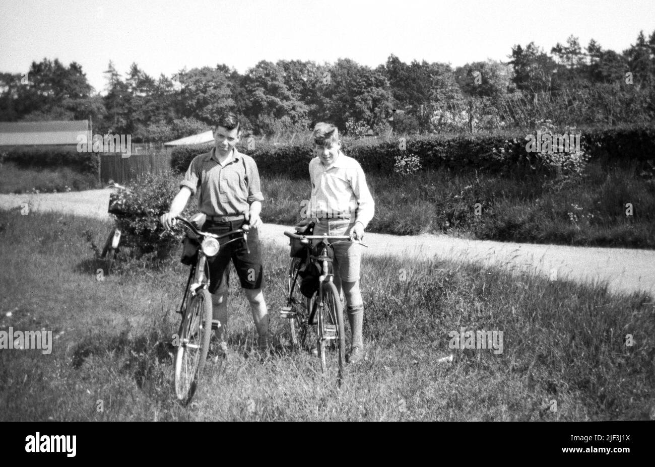 1930s, storico, due ragazzi adolescenti più anziani in piedi con le loro biciclette fuori in una zona erbosa accanto a una corsia di campagna, Newbury, Berks, Inghilterra, Regno Unito. Foto Stock