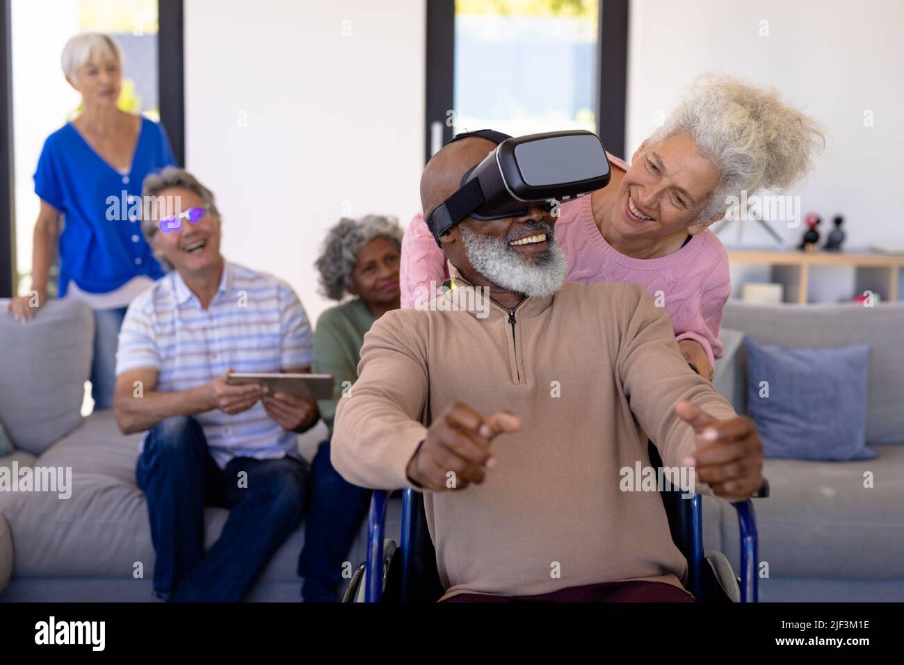 Anziani multirazziali che guardano un amico usando un simulatore di realtà virtuale mentre si siedono su una sedia a rotelle Foto Stock