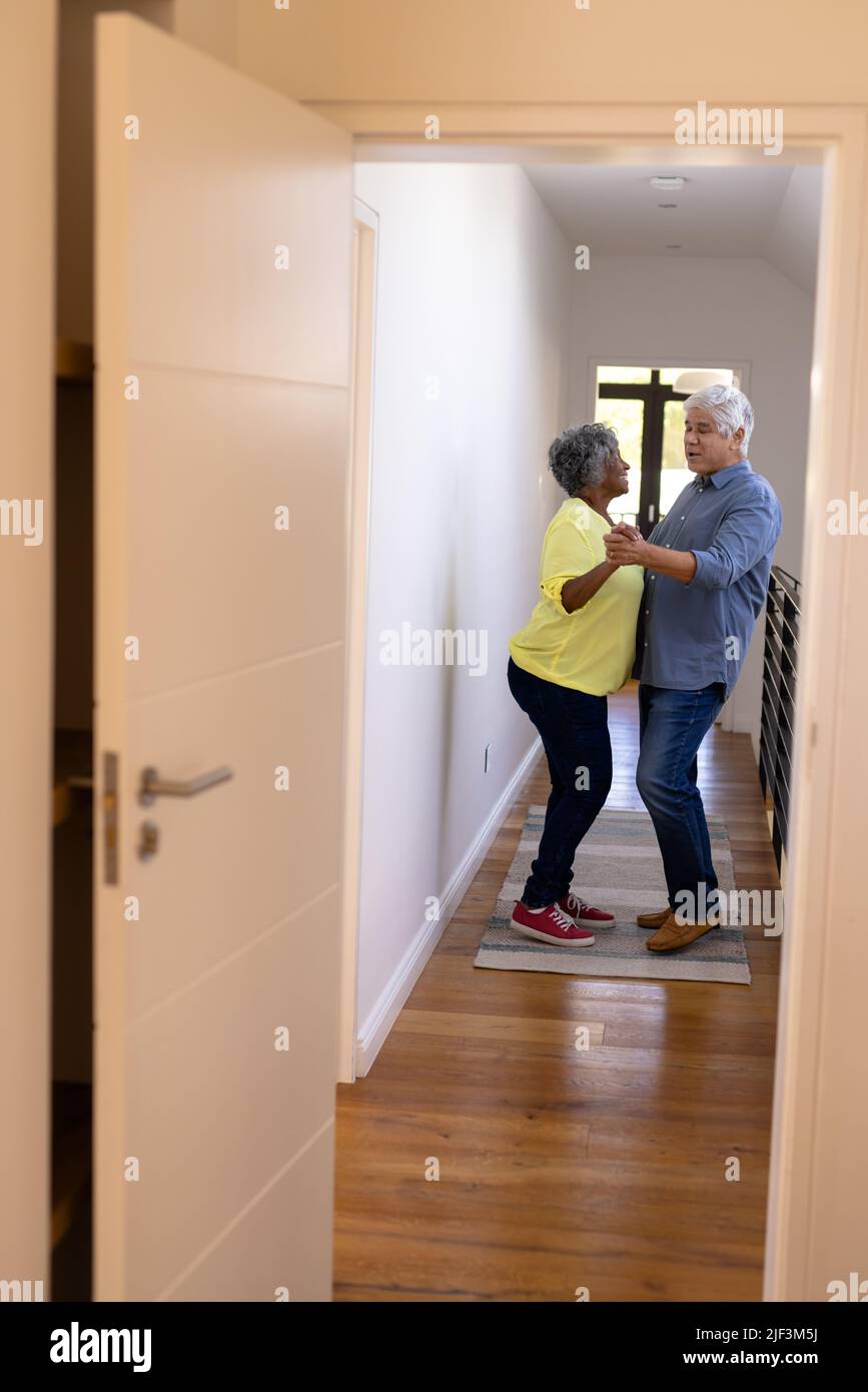 Allegri amici senior multirazziali che ballano in corridoio a casa di cura visto attraverso la porta Foto Stock