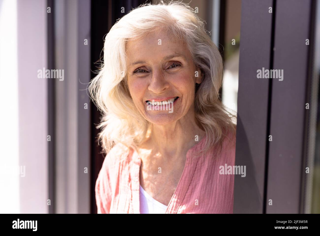 Primo piano ritratto di donna anziana caucasica sorridente con capelli ondulati dalla finestra a casa di cura Foto Stock