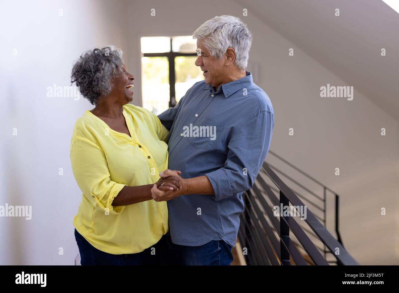 Amici anziani allegri multirazziali che si guardano mentre ballano in corridoio a casa di cura Foto Stock