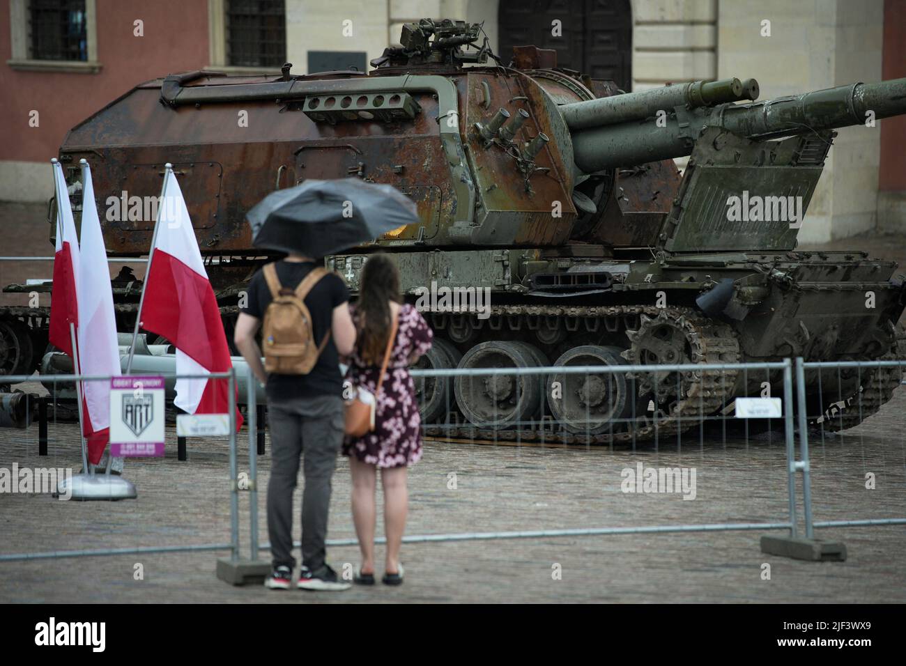 Una coppia che tiene un umbrealla si vede guardando un carro armato russo Howitzer vicino al Castello reale di Varsavia, in Polonia il 28 giugno 2022. Due Russi distrutti Foto Stock
