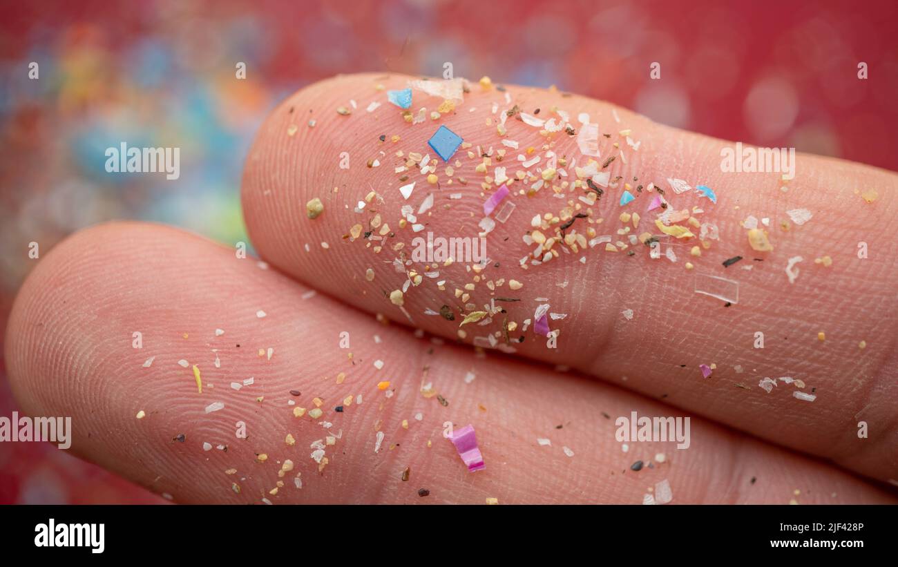 Micro particelle di plastica su un dito umano per la bilancia. Concetto di inquinamento idrico e riscaldamento globale. Foto Stock