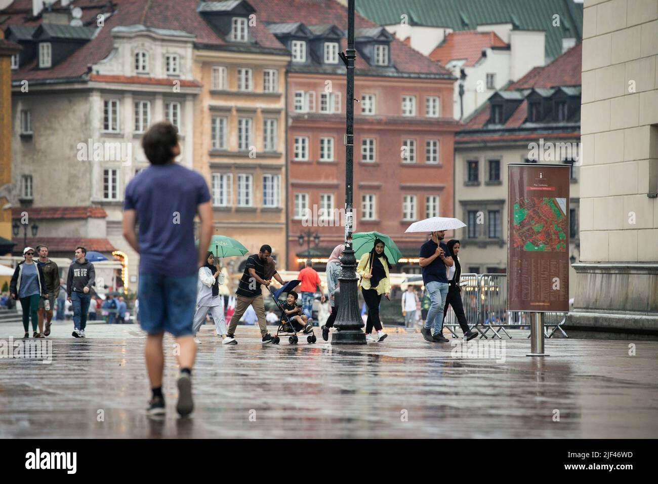 Un uomo spinge un buggy mentre un bambino ride un popolo cerca di cercare copertura dalla pioggia nella Città Vecchia di Varsavia, Polonia il 29 giugno 2022. Foto Stock