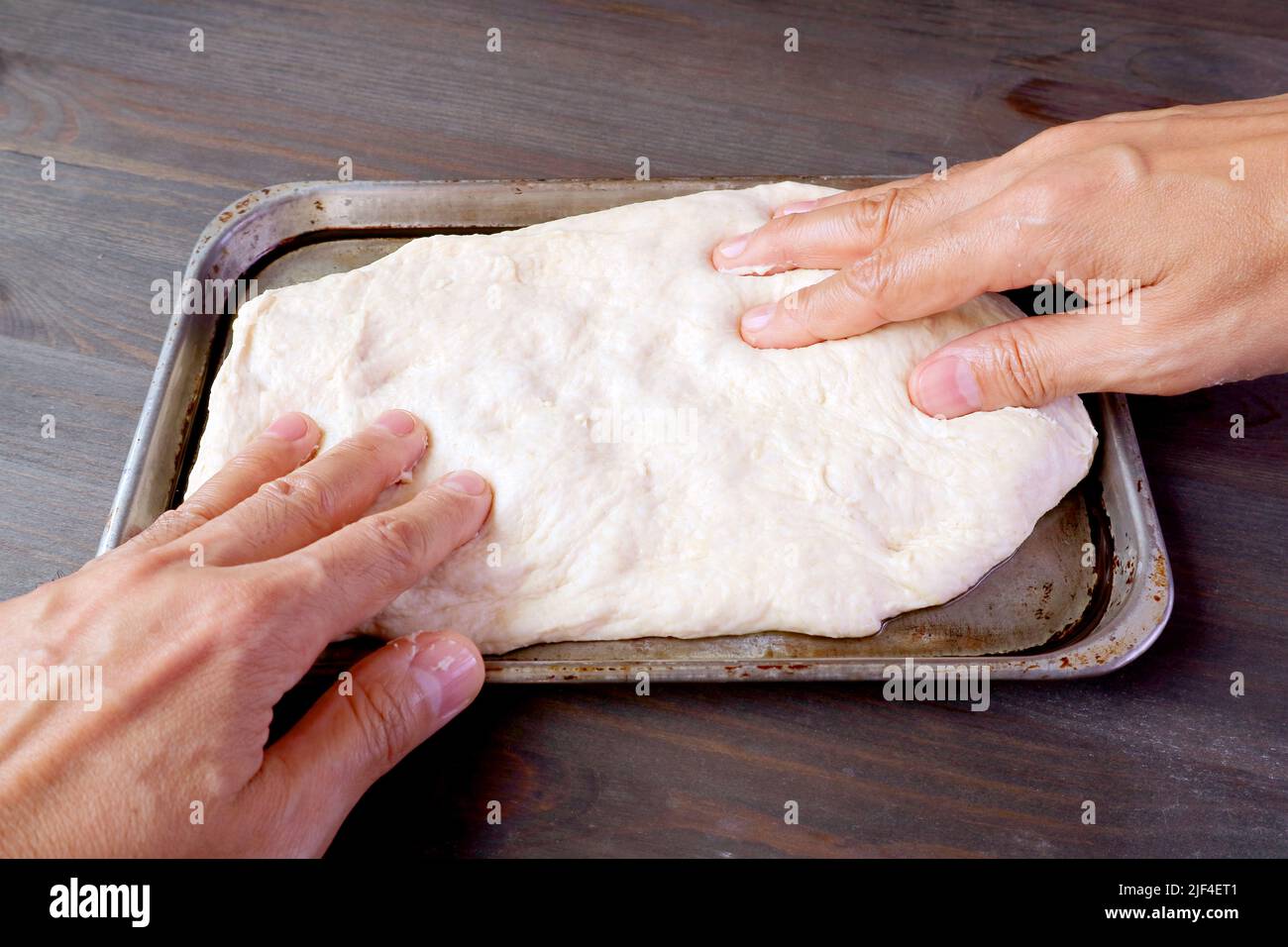 Le mani dell'uomo allungano l'impasto in una padella per cuocere pizza o pane Foto Stock