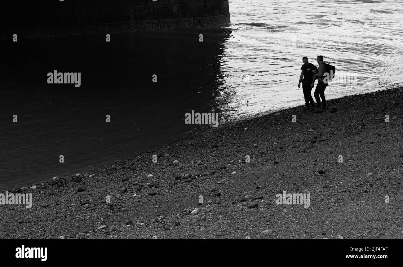 Silhouette di due uomini in cerca di oggetti interessanti o fango che si stira sulla riva del Tamigi a basso Tide sotto Blackfriars Railway Bridge Lon Foto Stock