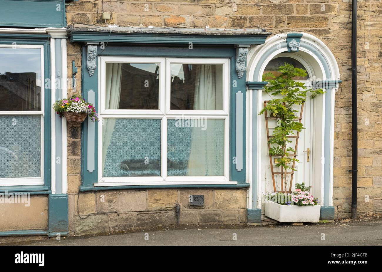 Una piantatrice di fiori in un vecchio lavello Belfast e glicine che crescono su un traliccio di fronte ad una porta casa Foto Stock