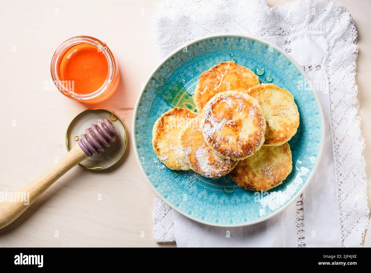 Pancake al formaggio casolare con miele su sfondo di legno chiaro, vista dall'alto. Foto Stock