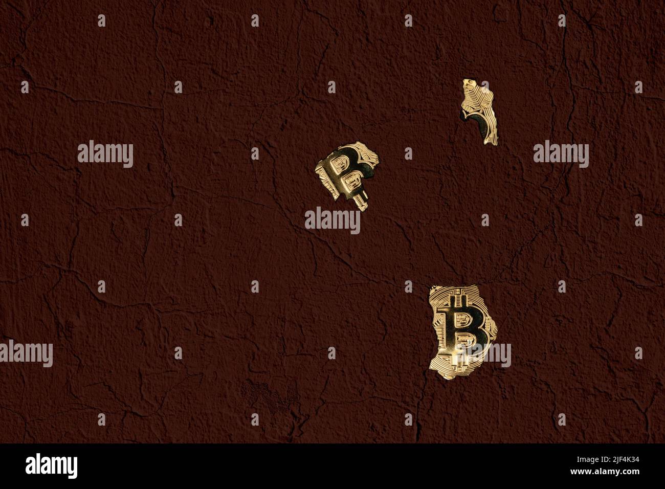 Parete marrone scuro con crepe e fori attraverso i quali sono parzialmente visibili tre monete bitcoin d'oro. Foto Stock