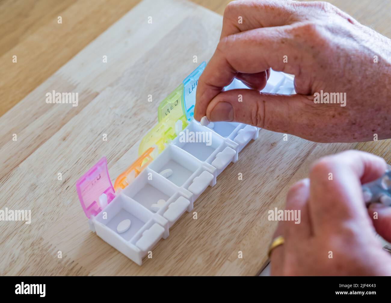 Un uomo che organizza settimanalmente compresse o pillole di farmaci in un organizzatore di pillole con giorni della settimana segnato, Regno Unito Foto Stock