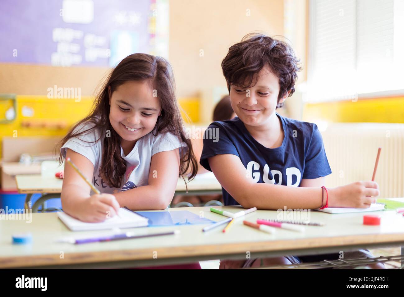 Due giovani bambini caucasici che si divertono a fare i compiti insieme in classe. Istruzione primaria. Concetto di ritorno a scuola. Foto Stock