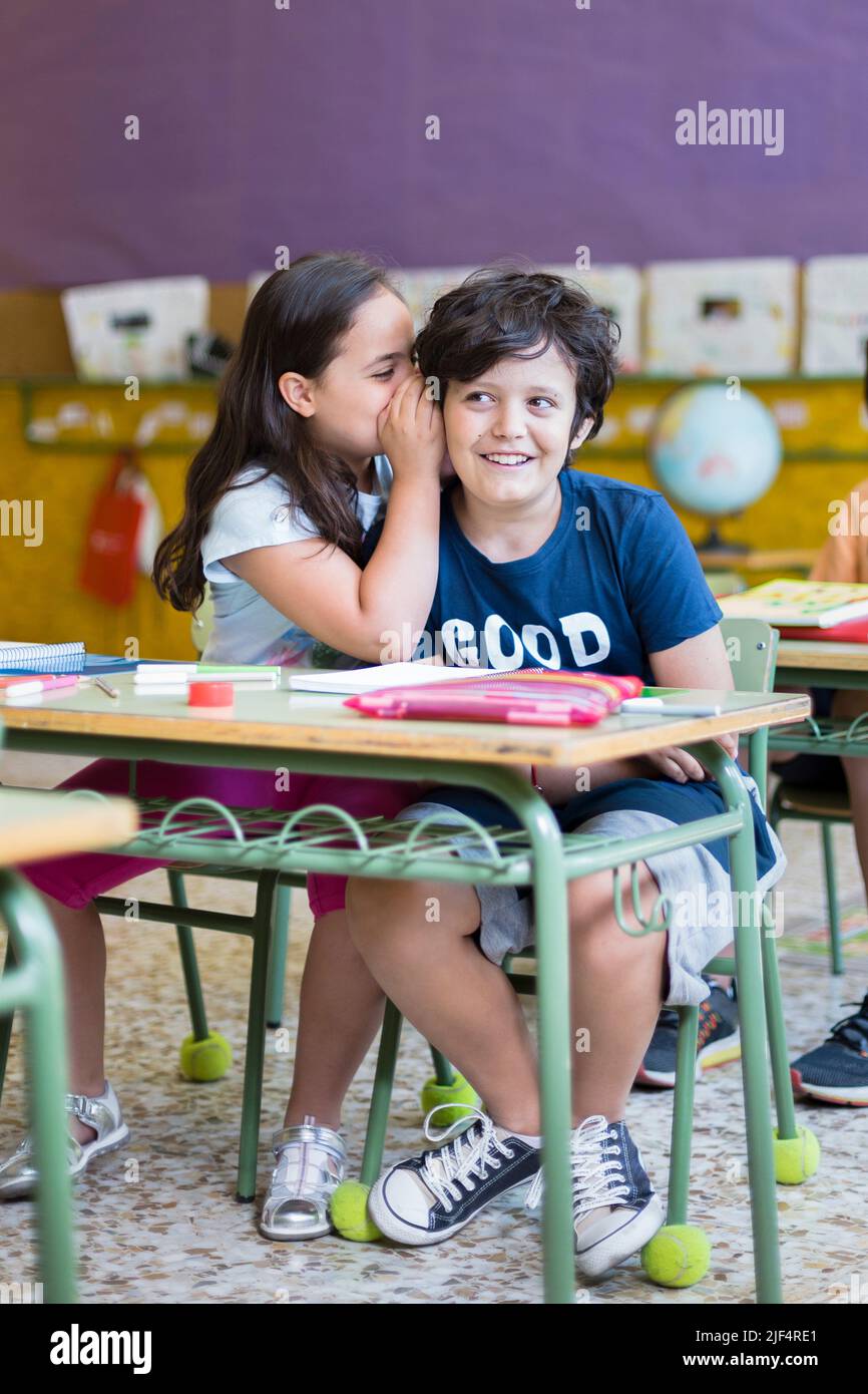 Due divertenti bambini caucasici che parlano in classe con distrarre. Istruzione primaria. Concetto di ritorno a scuola. Foto Stock