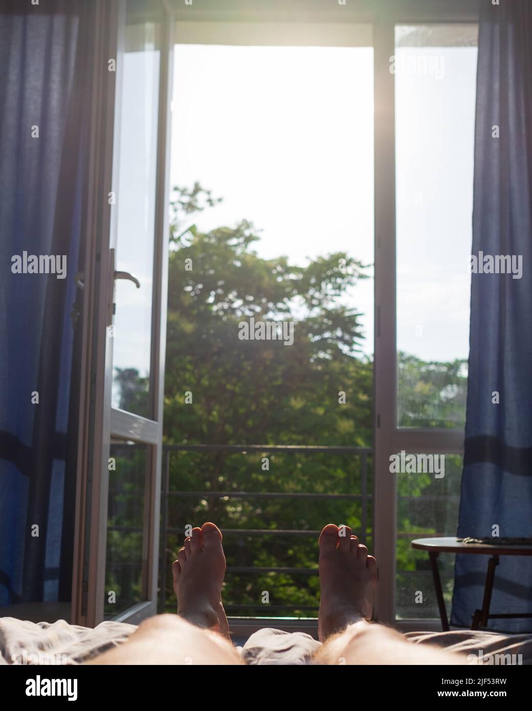Uomo gambe giacenti sul letto. Vista sulla finestra. È caldo all'interno senza aria condizionata. Foto Stock