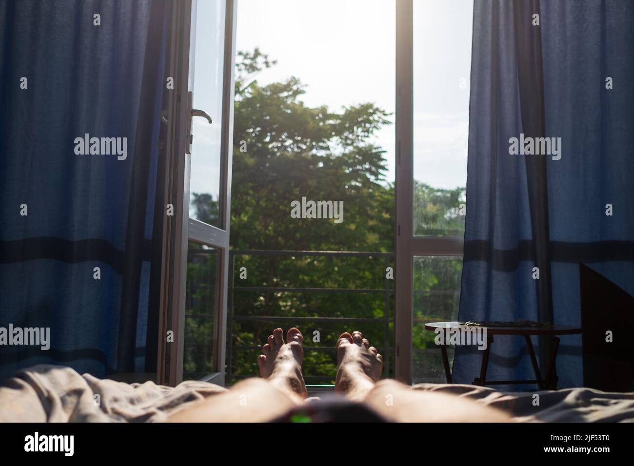 Uomo gambe giacenti sul letto. Vista sulla finestra. È caldo all'interno senza aria condizionata. Foto Stock