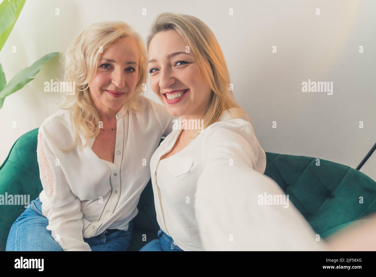 Indoor shot di due donne caucasiche correlate nel loro 40s indossare camicie bianche eleganti takinga selfie, abbracciandosi e sorridendo. Foto di alta qualità Foto Stock