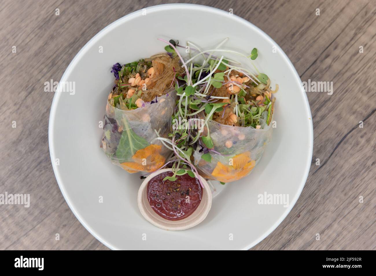 Rotolo di molla di stile vegetariano, tagliato a metà per mostrare gli ingredienti super verdi ed una salsa sana di immersione per quella dieta cosciente di nutrizione. Foto Stock