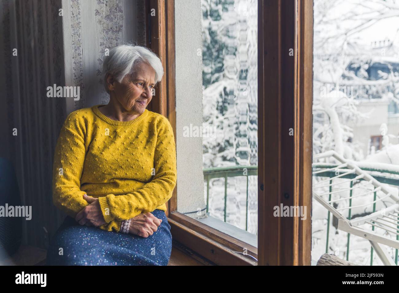 Donna caucasica anziana seduta sulla finestra-davanzale e guardando fuori cowboy colpo indoor senior people concetto. Foto di alta qualità Foto Stock