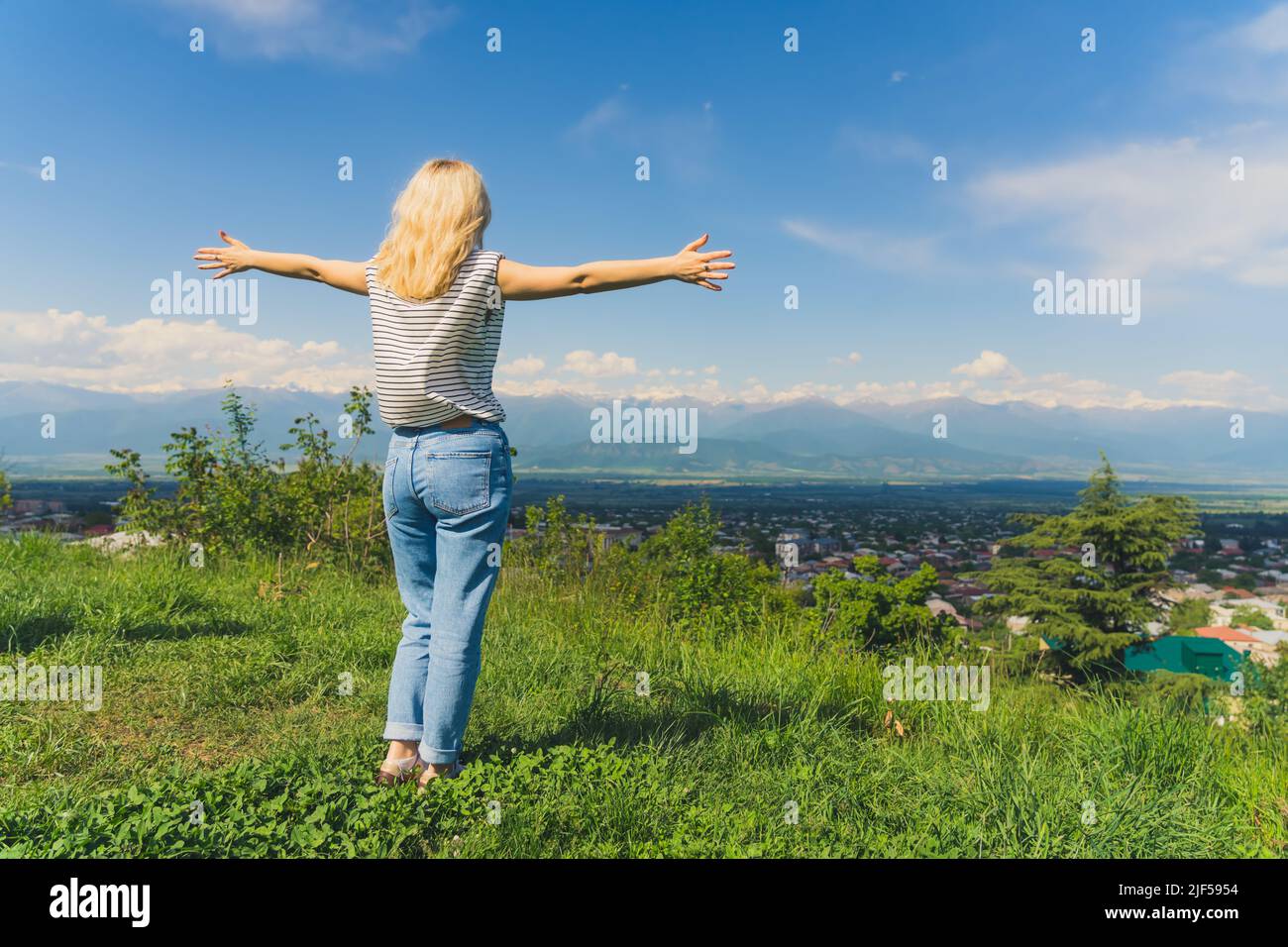 Ragazza bionda con le mani distese su una vista meravigliosa della valle di Alazani e delle montagne del Caucaso in Georgia. Colpo pieno. Foto di alta qualità Foto Stock