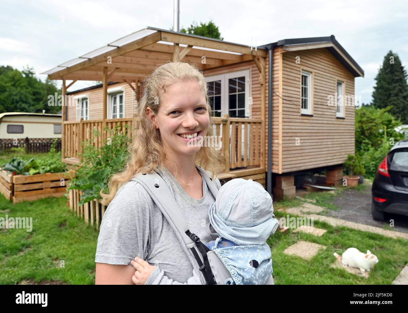 Waldbronn, Germania. 27th giugno 2022. Larissa Pferdmenges si trova con il bambino di fronte alla sua piccola Casa al campeggio Albtal. Ci sono ora piccole case in tutta la Germania. Non ci sono ancora molti, perché i lotti adatti di terra sono rari. (A dpa-Korr 'vivere - le case minuscoli sono una tendenza ma rimangono un posticino ') accreditamento: Uli Deck/dpa/Alamy Live News Foto Stock