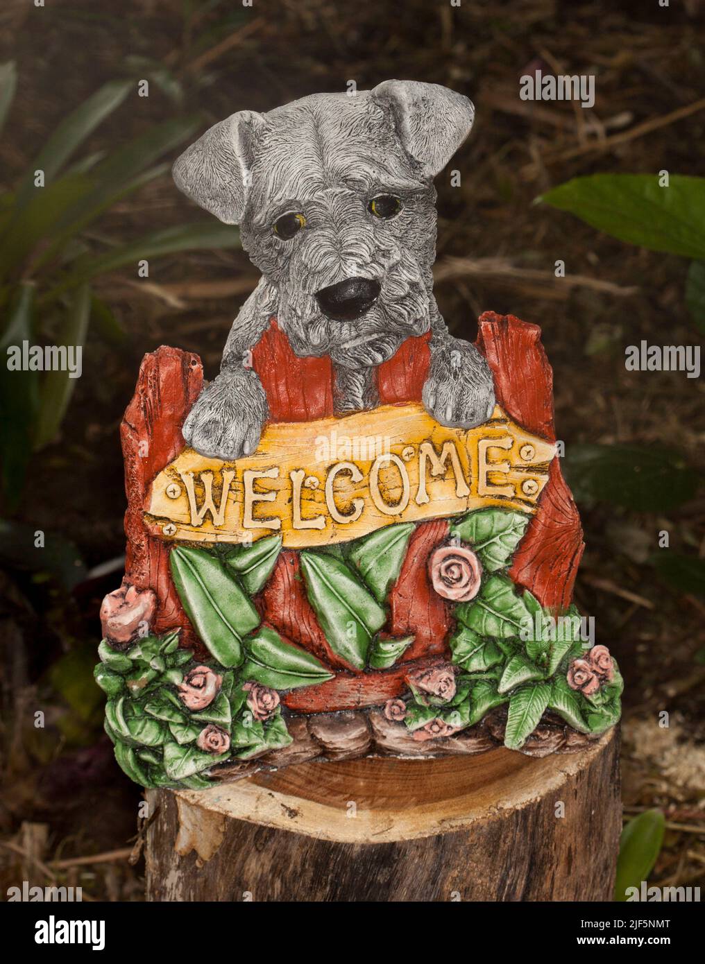 Insolita e attraente ornamento in cemento - Highland Terrier cane con zampe sul cartello di benvenuto circondato da rose e foglie Foto Stock