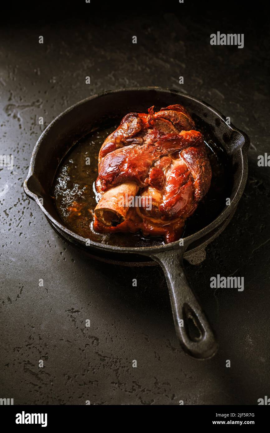 Cucina tradizionale tedesca - Pasta di maiale arrosto eisbein (Schweinshaxe) in padella di ferro su sfondo nero Foto Stock